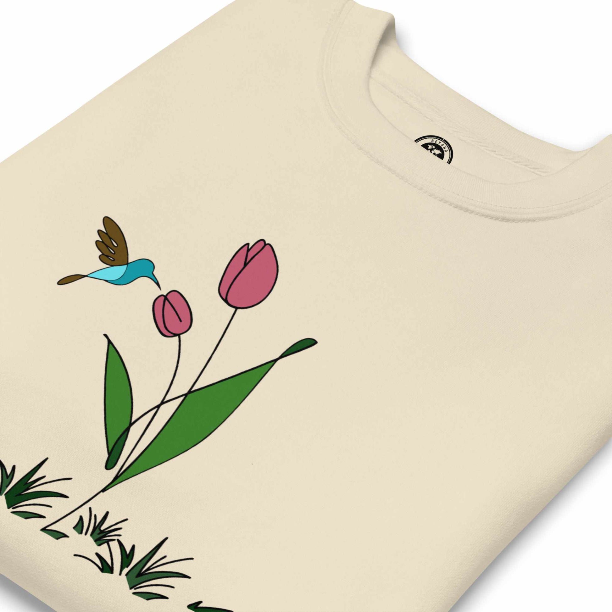 Folded Beige sweatshirt with a floral design featuring tulips and hummingbird on a white background