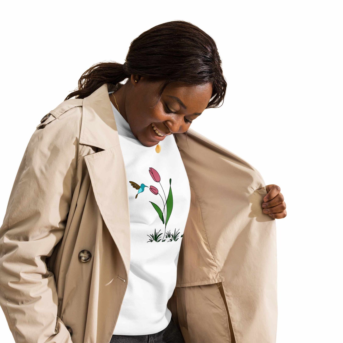 Happy Woman wearing a beige trench coat over a white sweatshirt with floral design featuring tulips and a hummingbird on a white background