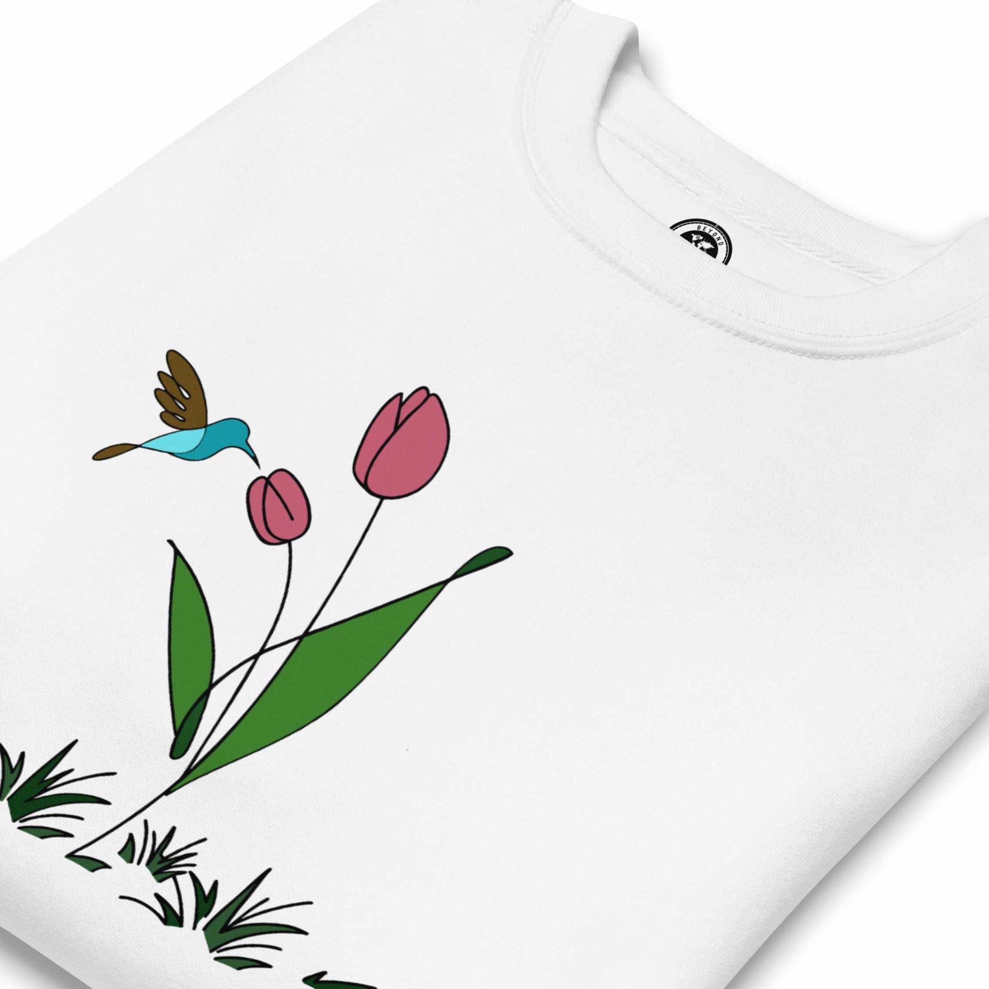 Folded White sweatshirt with a floral design featuring tulips and a hummingbird on a white background.