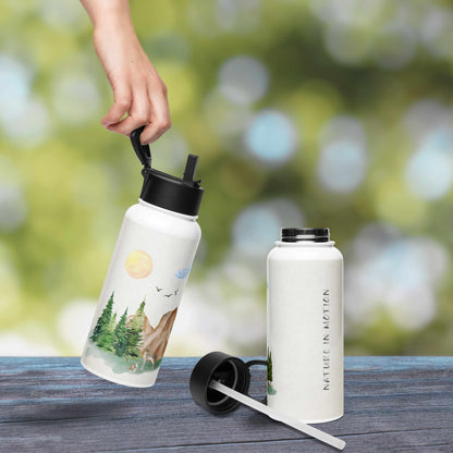 White water bottle with nature-themed illustration of a forest scene with trees, mountain, rocks, and animals on a wooden surface with a blurred green background.