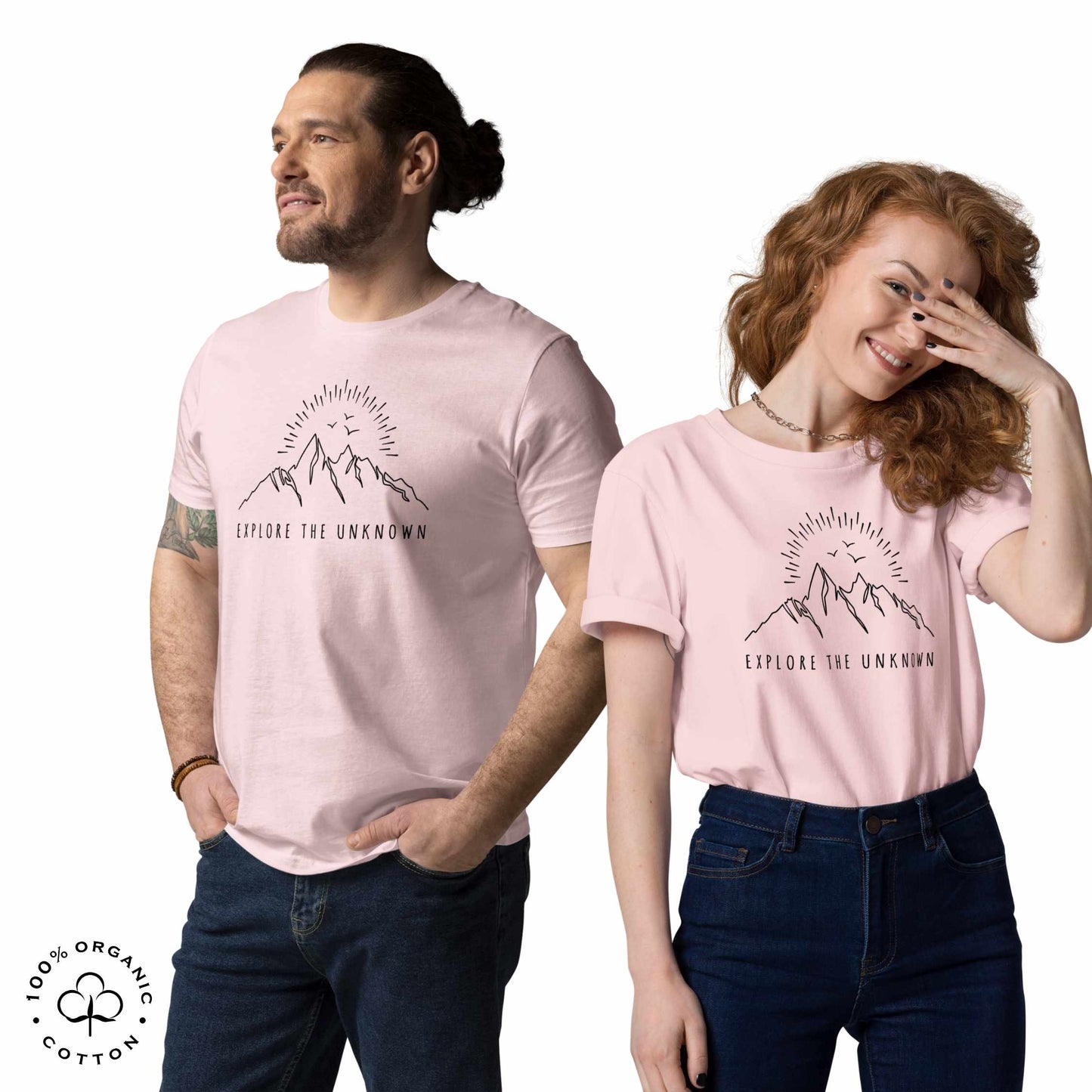 happy man and woman wearing pink organic cotton t-shirt with mountain, sun and birds graphic and 'Explore the Unknown' text on a white background.