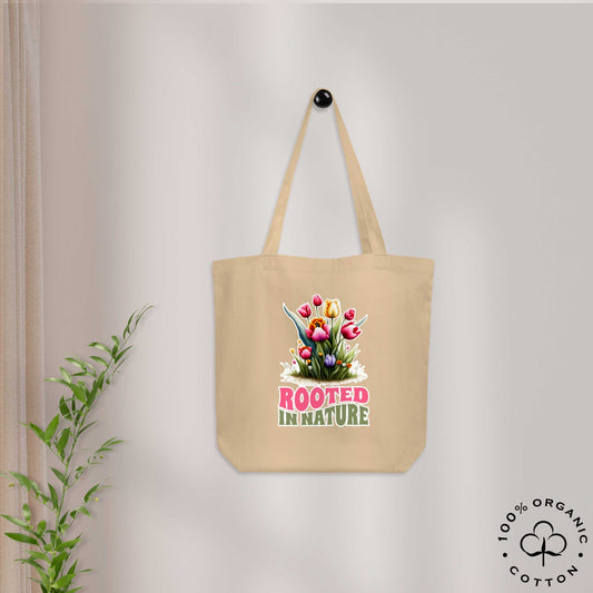 Beige organic cotton tote bag with floral design and 'Rooted in Nature' text on a light gray wall.