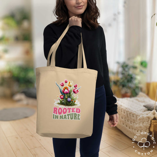 Woman at home holding a beige organic cotton tote bag with rooted flowers design and 'Rooted in Nature' text