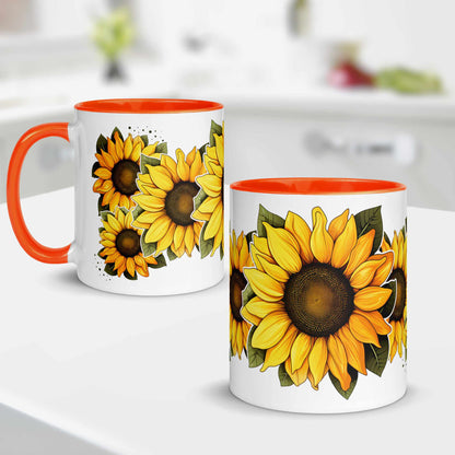 Two white mugs with orange interior and rim, featuring sunflower designs on a blurred kitchen background.