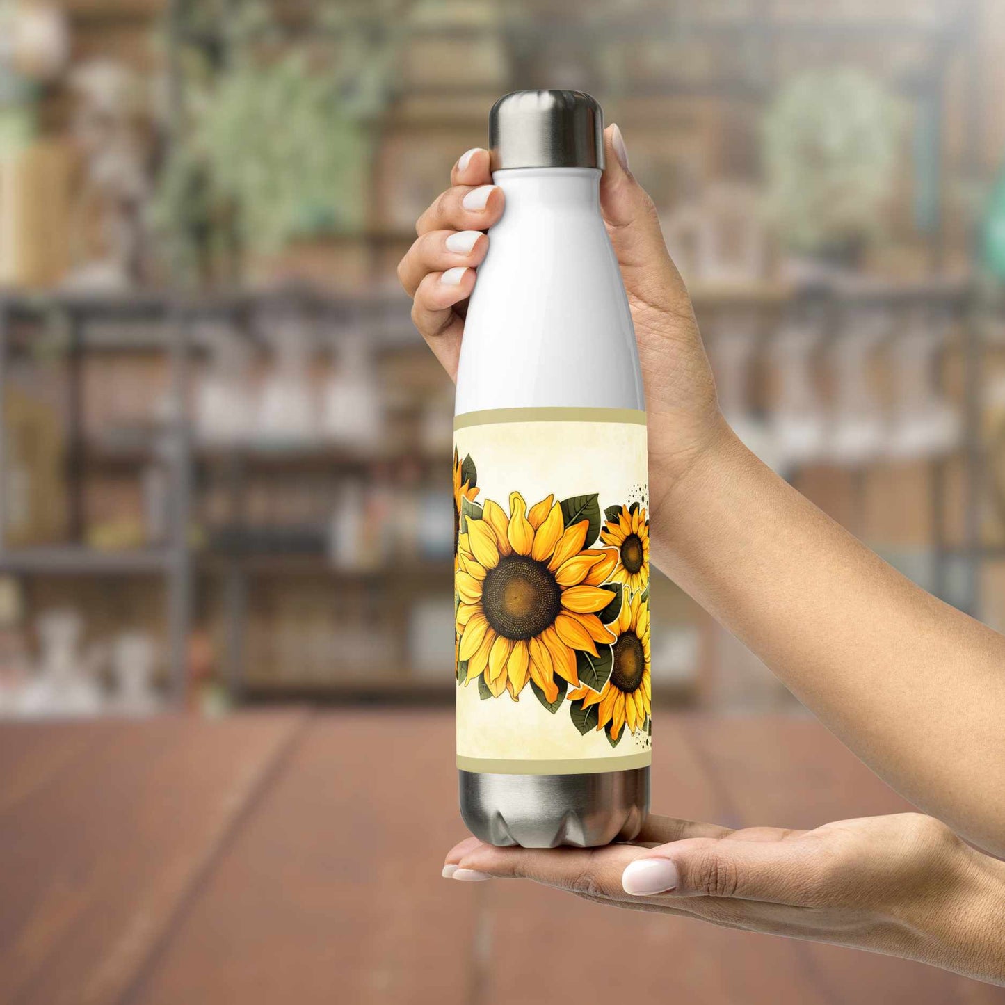 Person holding a water bottle stainless steel with sunflower design in a blurred indoor setting