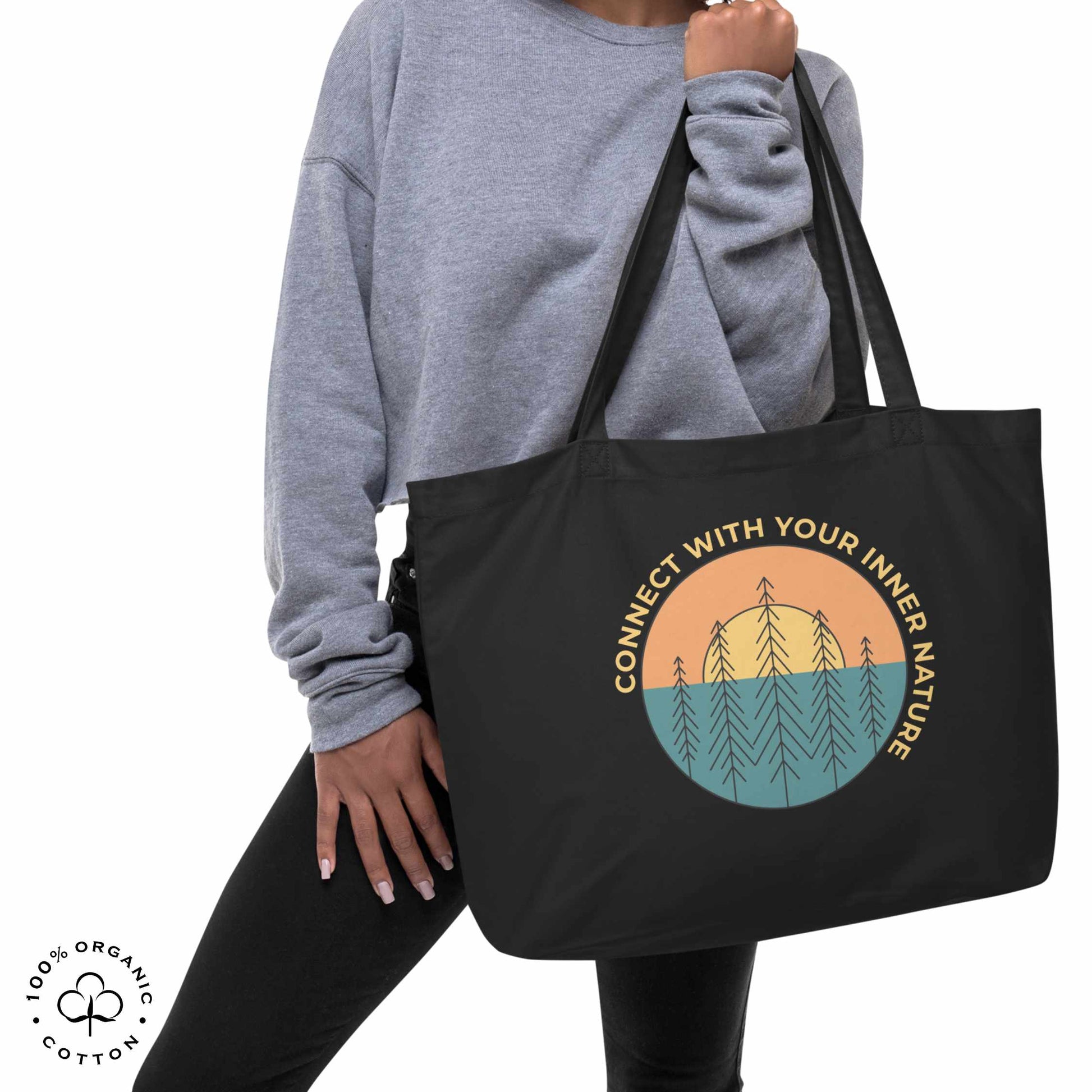 Woman holding black organic cotton tote bag with nature-themed design featuring sun and trees and 'Connect with Your Inner Nature' text on a white background.