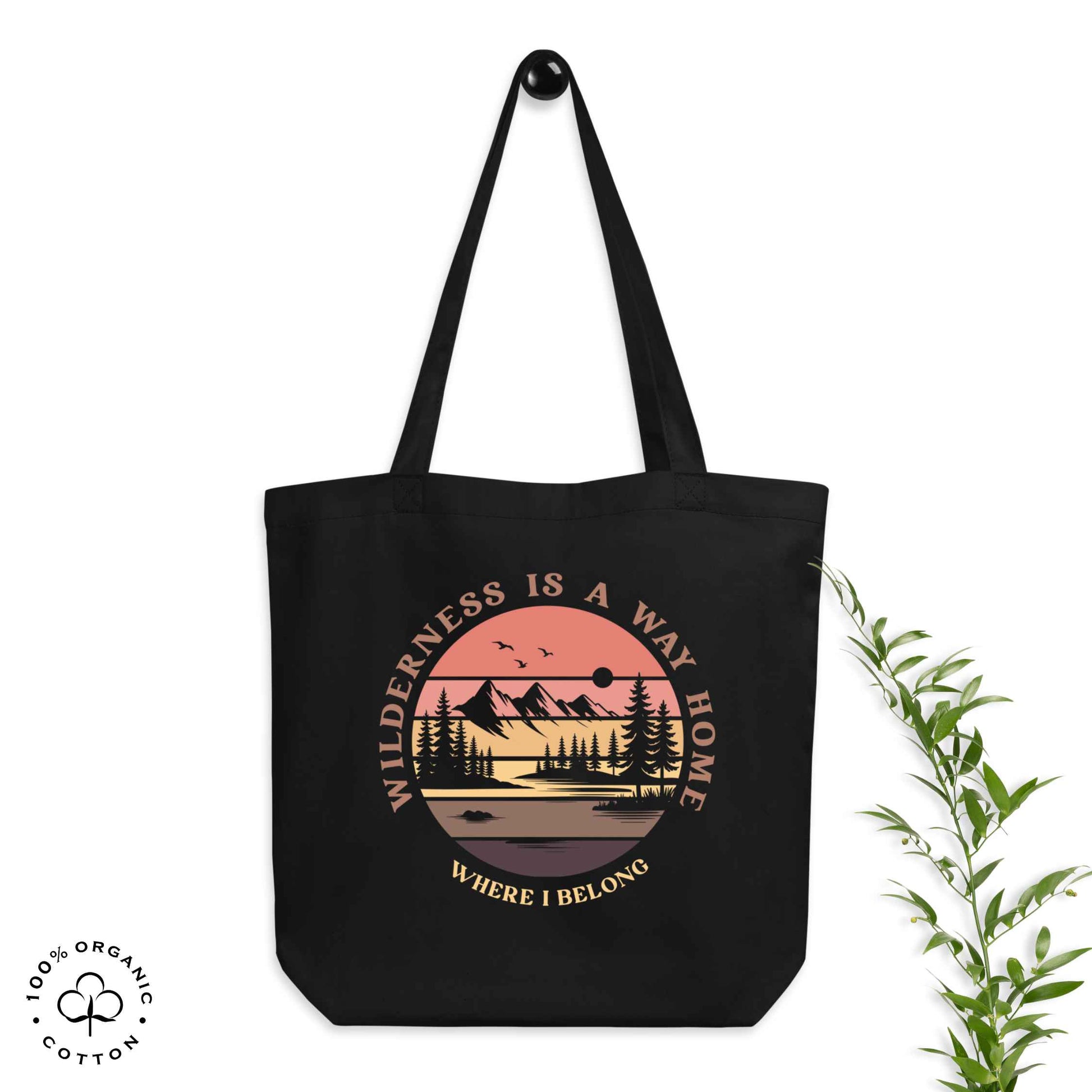 Black organic cotton medium tote bag with nature-themed design: forest, trees, sun, lake. 'Wilderness is a Way Home, Where I belong' text. 