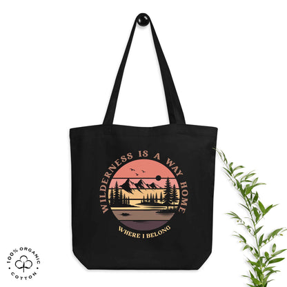 Black organic cotton medium tote bag with nature-themed design: forest, trees, sun, lake. 'Wilderness is a Way Home, Where I belong' text. 