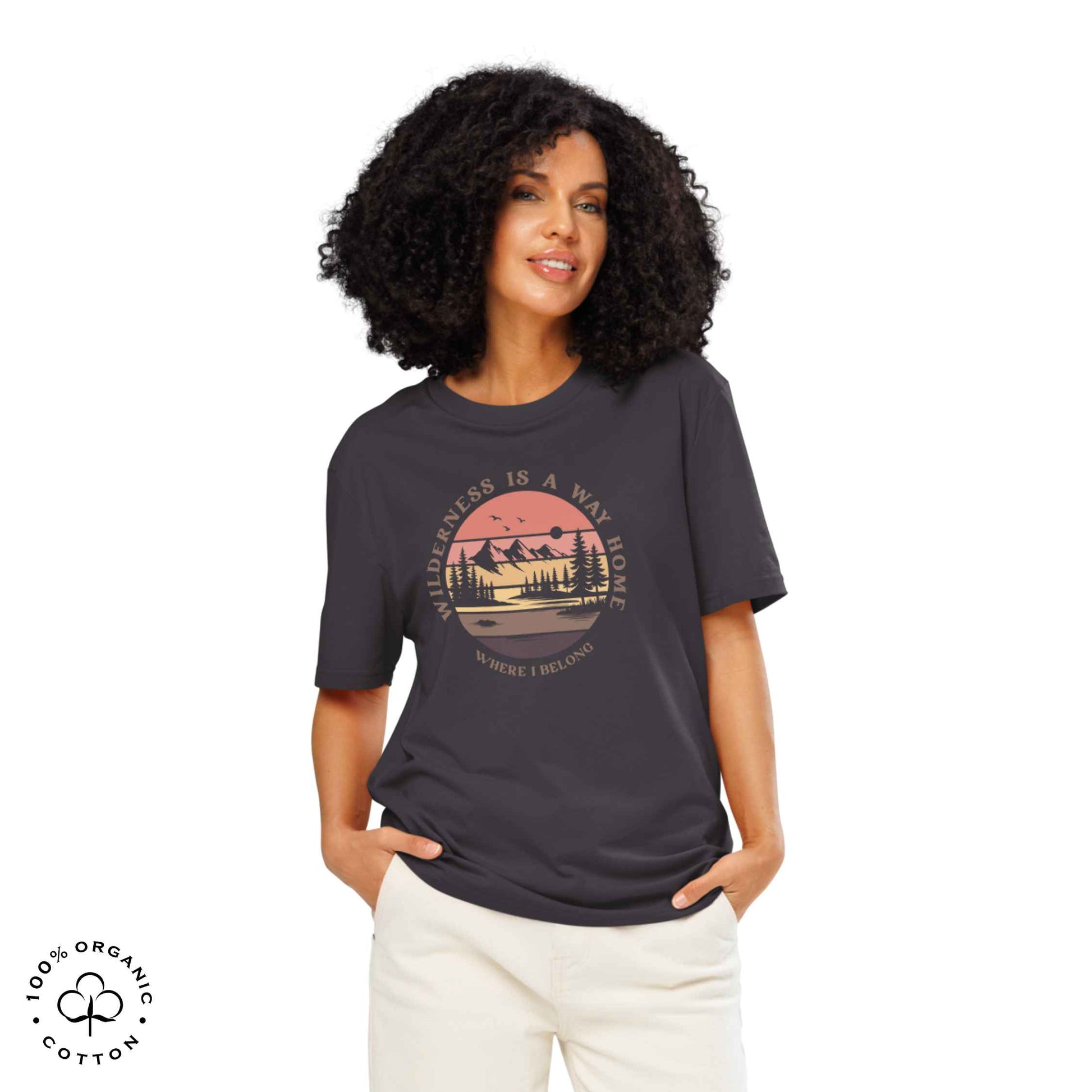 Woman wearing Eco-friendly t-shirt in organic cotton, anthracite, with graphic featuring a nature theme: mountains, trees, sun and the bold phrase “wild nature is the way home, where I belong”.