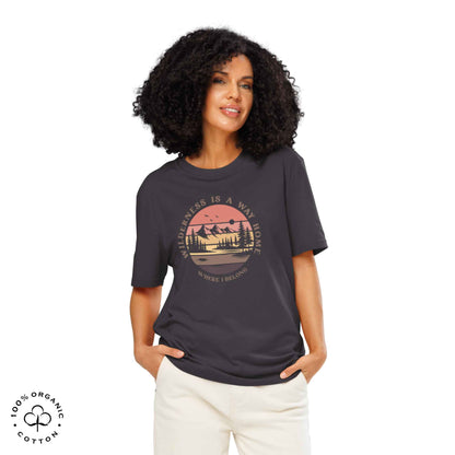 Woman wearing Eco-friendly t-shirt in organic cotton, anthracite, with graphic featuring a nature theme: mountains, trees, sun and the bold phrase “wild nature is the way home, where I belong”.